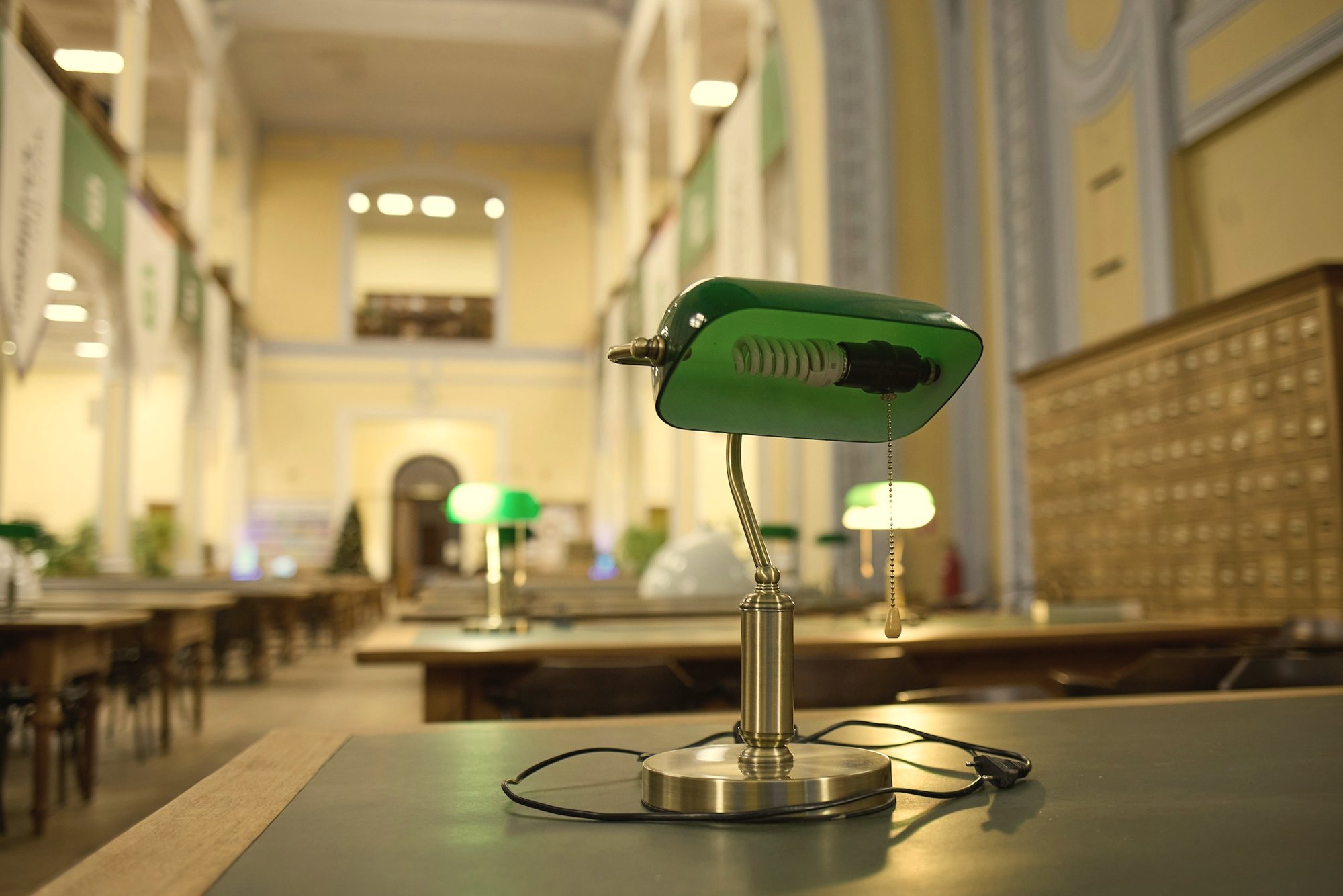 A green desk lamp on a table in a reading room